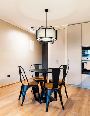 Un espace repas moderne avec une table ronde, quatre chaises, un luminaire suspendu et un plancher en bois.