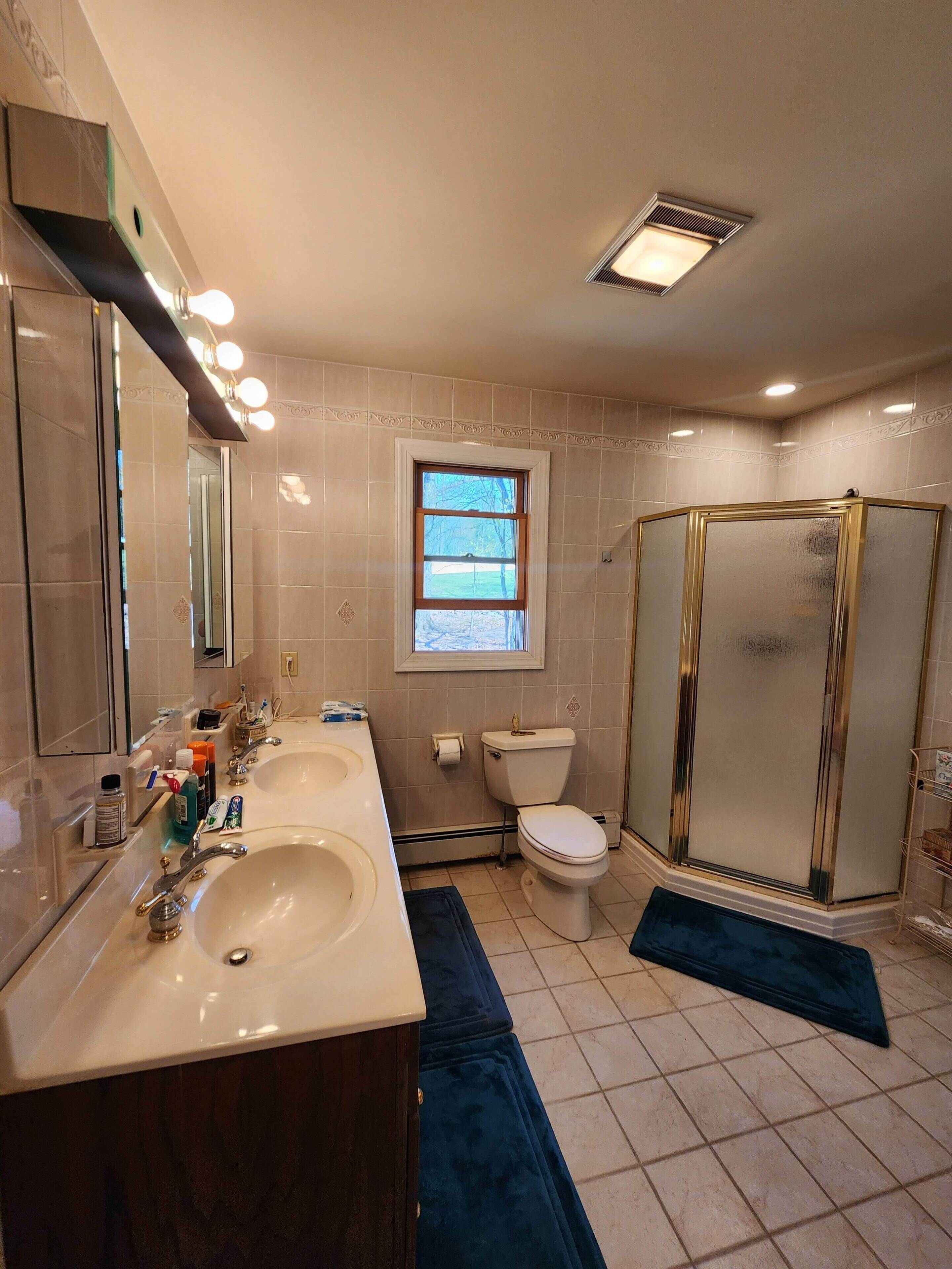 A bathroom with two sinks, a toilet, a shower, and a window.