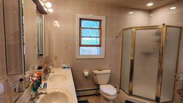 A bathroom with two sinks, a toilet, a shower, and a window.