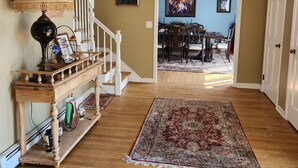 A hallway with a wooden floor, a staircase, a dining area with a chandelier, and a door on the right.