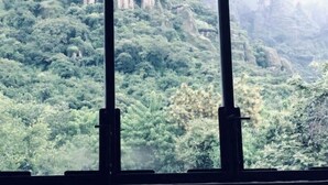 Ein Blick durch ein Fenster auf eine Berglandschaft mit dichtem Grün und steilen Felsen.