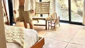 Ein Schlafzimmer mit Bett, Stuhl, Tisch und einem fensterbepflanzten Fenster.