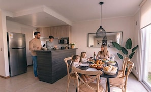 A modern kitchen with a central island, a dining area with wooden chairs, and a large window providing natural light.