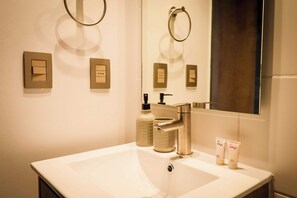A bathroom with a white sink, a mirror, a towel ring, a soap dispenser, and two toiletry bottles. - Central Apartment Near Metro & Iconic Sights w/ (Santiago)