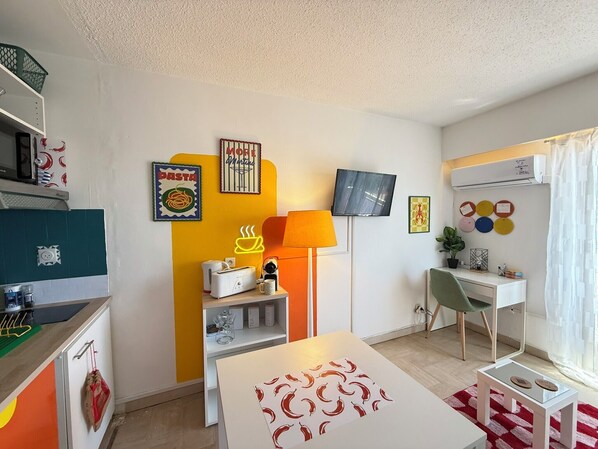A modern living room with a TV, sofa, coffee table, and a desk with a chair. - Studio coloré & fonctionnel – proche gare, plages & vieille ville (Antibes)
