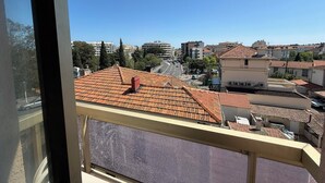 Ein Balkon mit Ziegeldach, mit Blick auf eine Stadtlandschaft aus verschiedenen Gebäuden und einem klaren Himmel.