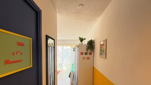 Ein Flur mit Spiegel, Tür, Kühlschrank und einem Fenster mit Vorhängen.