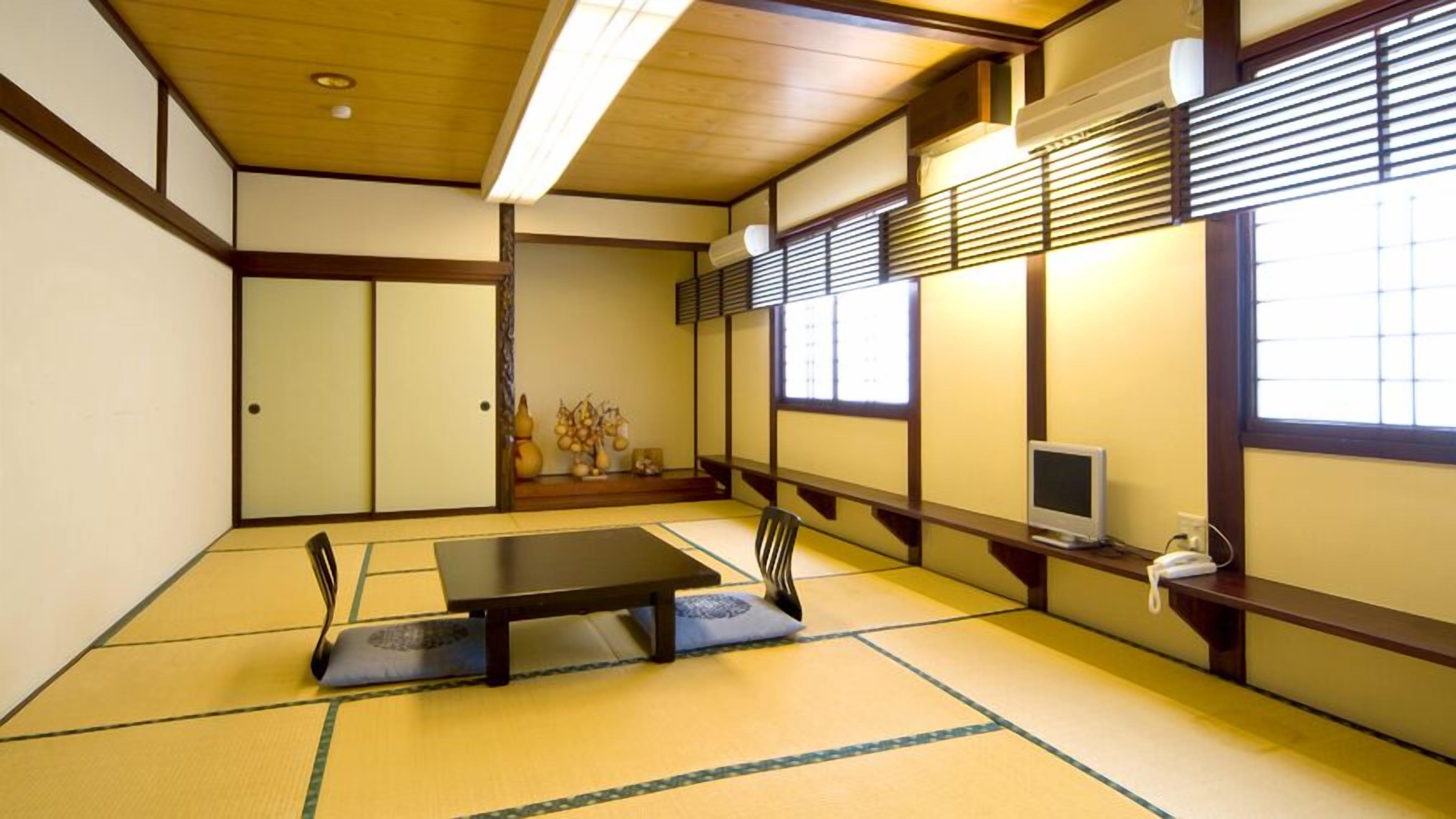 Ein traditioneller japanischer Raum mit Tatami-Bodenbelag, einem niedrigen Tisch, Schiebetüren und einem Fernseher auf einem Regal.