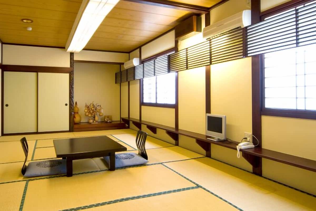 A traditional Japanese room with tatami flooring, a low table, sliding doors, and a TV on a shelf.