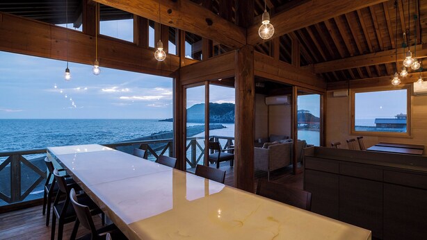 Una habitación amplia con una gran mesa blanca, vigas de madera y vistas al mar.