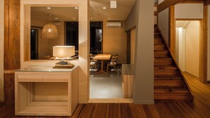 Un interior moderno con una escalera de madera, un comedor y un escritorio con frentes de vidrio y una lámpara.