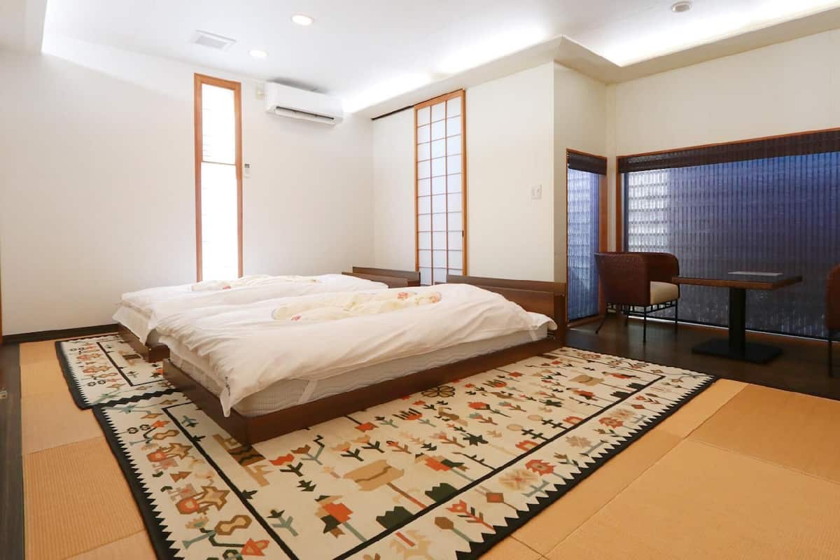 A hotel room with a large bed, two chairs, a small table, a tatami mat, and a sliding door.
