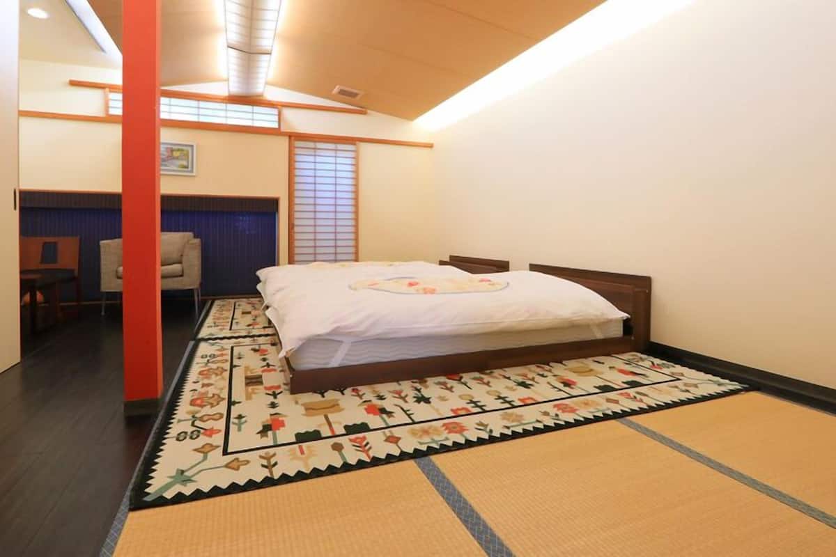 A traditional Japanese-style room with tatami flooring, a bed with a floral bedspread, a desk, and a shoji screen.