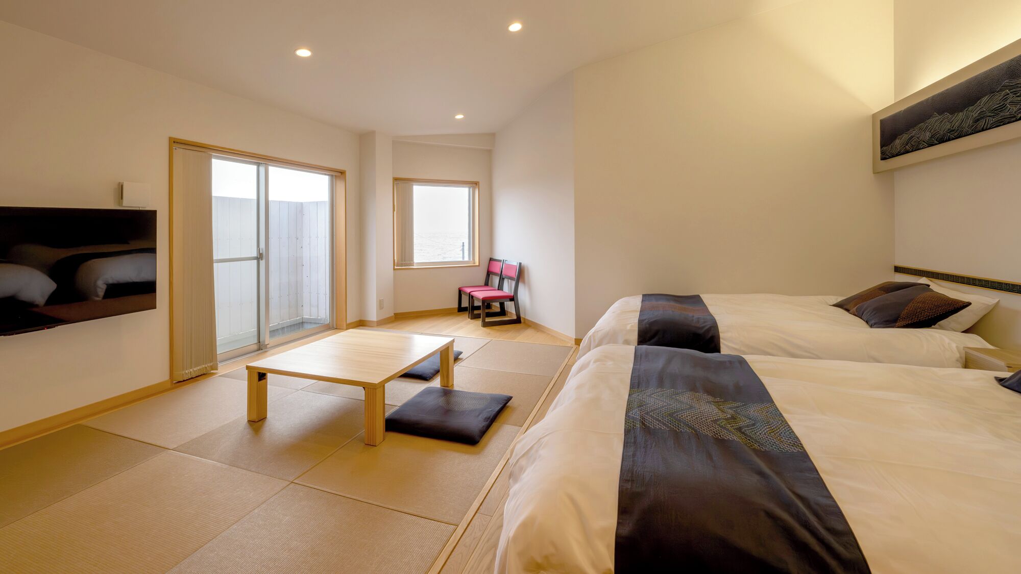 Ein Hotelzimmer mit zwei Betten, einem kleinen Tisch, einem Stuhl und einer Balkontür.