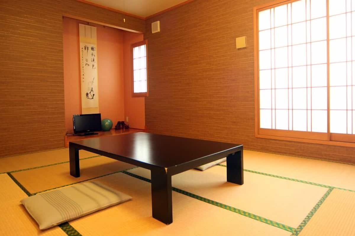 A tatami mat room with a low table, a tatami mat pillow, a television, and a shoji screen.