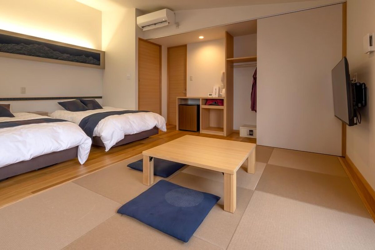 Ein Hotelzimmer mit zwei Betten, einem kleinen Tisch, einem Kleiderschrank und einer Klimaanlage.