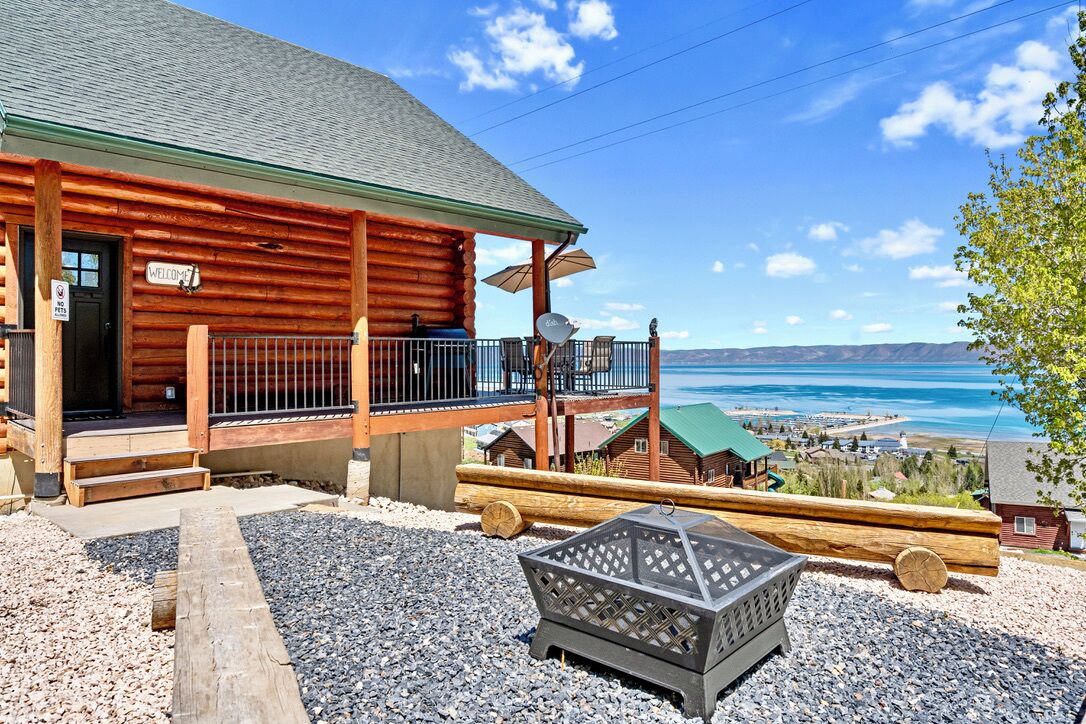 A log cabin with a balcony, a welcome sign, and a view of the ocean.