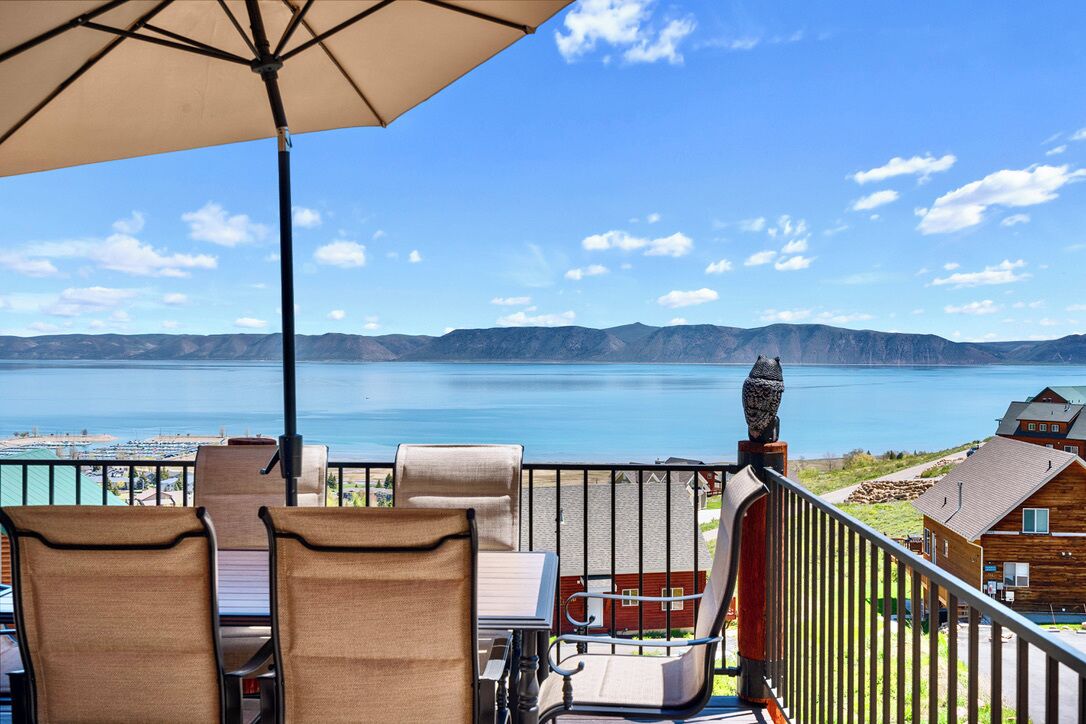Ein Balkon mit Stühlen und Sonnenschirm mit Blick auf einen See und Berge.