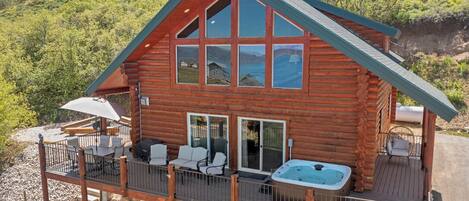 A log cabin with a deck, outdoor seating, and a hot tub.