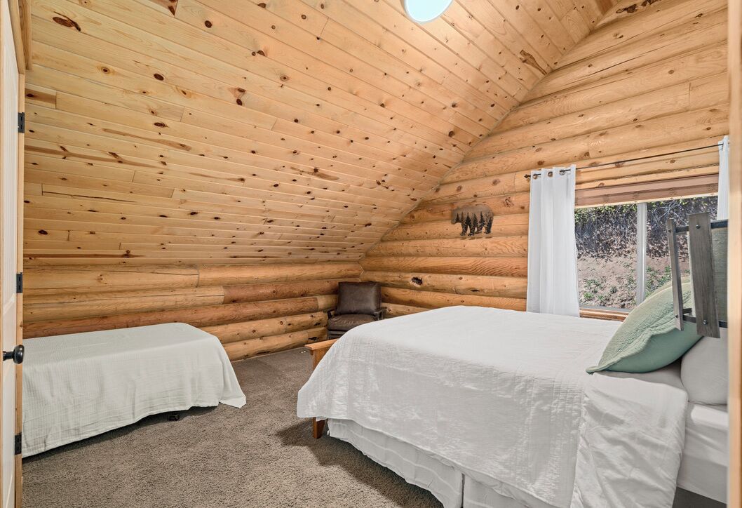 Un dormitorio tipo cabaña de madera con dos camas, una ventana con cortinas y una decoración con osos en la pared.
