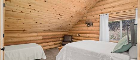 Un dormitorio tipo cabaña de madera con dos camas, una ventana con cortinas y una decoración con osos en la pared.