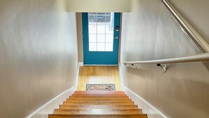 Una escalera de madera con barandilla que lleva a una puerta con ventanal.
