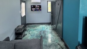 Huoneessa on marmorilattia, seinälle asennettu televisio, liukuovi ja harmaa sohva.