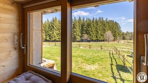 Une cabane en bois dotée d’une grande fenêtre, d’un banc et offrant une vue sur une zone boisée.