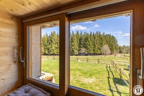Eine Holzhütte mit großem Fenster, einer Bank und Blick auf einen bewaldeten Bereich.