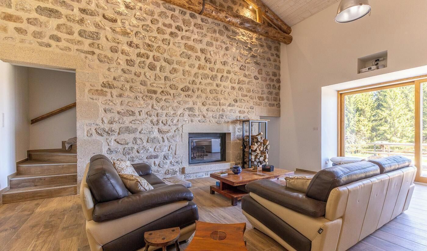 Una sala de estar con paredes de piedra, chimenea, sofás de cuero y suelo de madera.