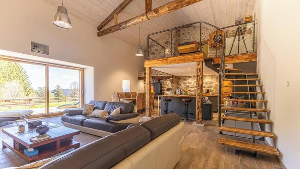 Un vaste espace de vie avec une grande fenêtre, un escalier en bois et une cuisine moderne.