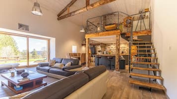 Una zona d'estar àmplia amb un gran finestral, una escala de fusta i una cuina moderna.