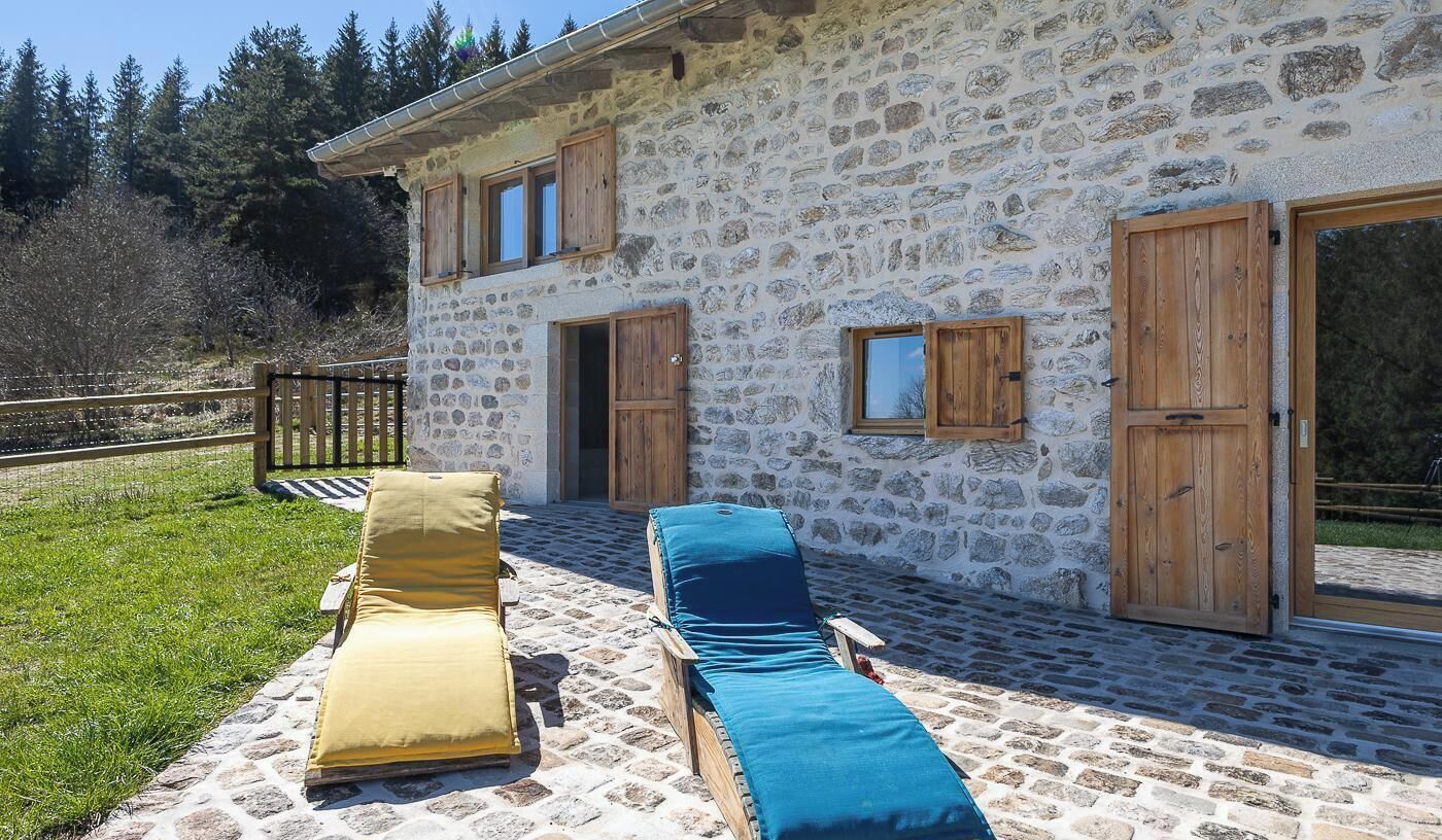 A stone building with two wooden doors, a balcony with two sun loungers, and a grassy area.