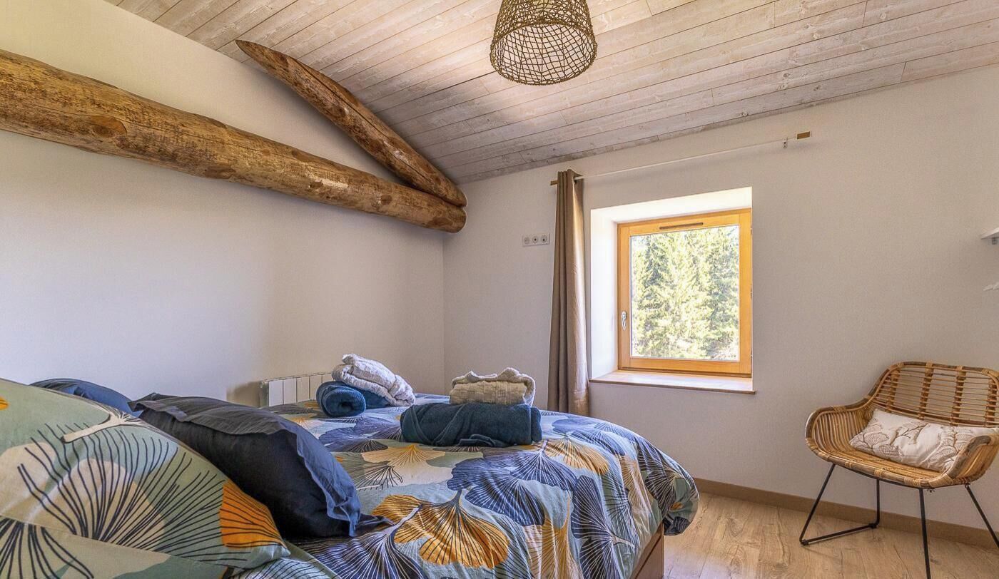 Un dormitorio con una cama, un ventanal, una silla y techo de madera.
