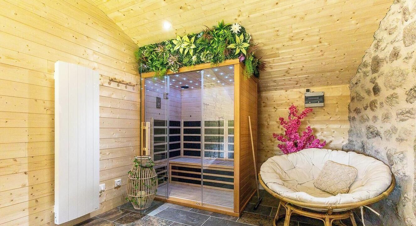Uma sala de sauna com paredes de madeira, porta de vidro, cadeira de vime e um arranjo decorativo de plantas.