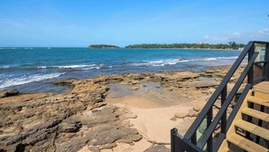 Una playa rocosa con una terraza de madera y vista al océano.