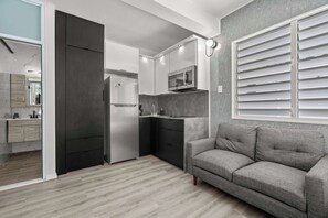 A modern kitchen with a built-in microwave, a refrigerator, and a grey sofa in a living area.