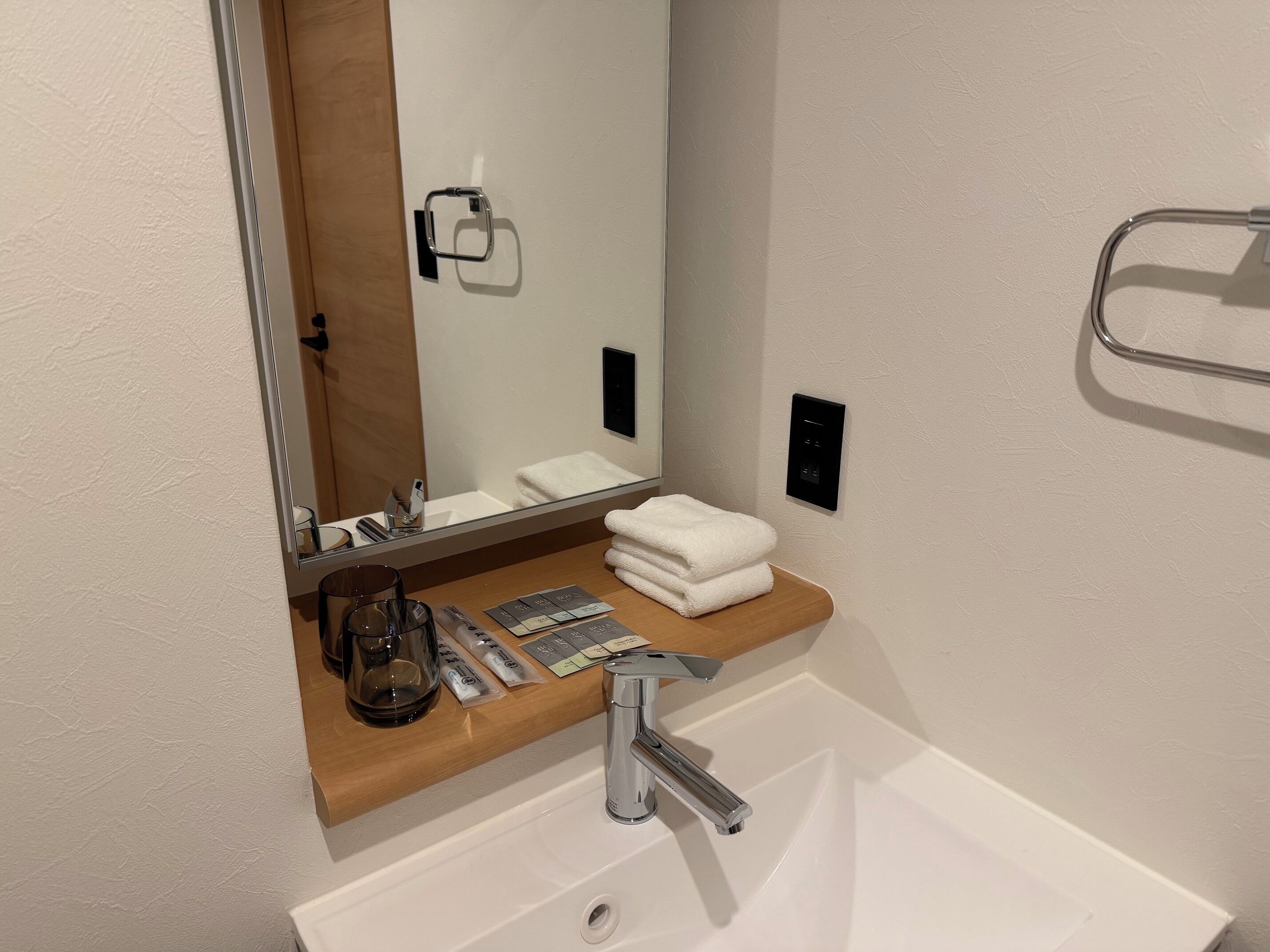 Un bagno moderno con un lavandino bianco, uno specchio, un porta asciugamani e un piano d'appoggio in legno.