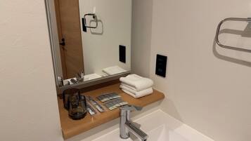 Un bagno moderno con un lavandino bianco, uno specchio, un porta asciugamani e un piano d'appoggio in legno.