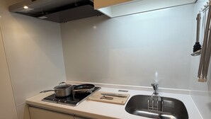 A compact kitchen with a stove, pots, a frying pan, a knife block, and a sink. - reside global kumamoto (Kumamoto)