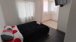 Un dormitorio con cama, televisión montada en la pared y ventana con cortinas.