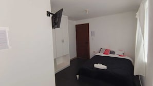 Una habitación pequeña y limpia con cama, armario, puerta y televisor montado.