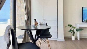A modern room with a round table, a potted plant, a TV, and a view of the ocean.