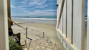 A beach view from a building with a stone staircase leading to a sandy area.