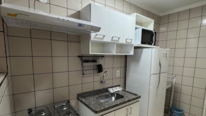 A compact kitchen with a gas stove, a microwave, a refrigerator, and a sink. - IL Locações di Roma Fiori (Caldas Novas)