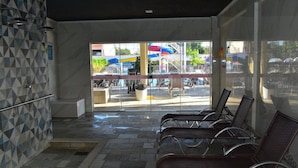 A waiting area with chairs, a tiled wall, and a view of an outdoor area with umbrellas and chairs. - IL Locações di Roma Fiori (Caldas Novas)
