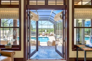 A glass door leading to a pool area with wicker furniture and a view of the landscape. - Gated Riverfront Estate, Heated Pool, Private Dock, Boat Lifts, Amazing Views, Sauna, Elevator (St. Augustine)