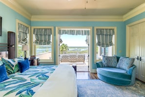 A bedroom with a bed, a blue armchair, and a view of the outdoors. - Gated Riverfront Estate, Heated Pool, Private Dock, Boat Lifts, Amazing Views, Sauna, Elevator (St. Augustine)