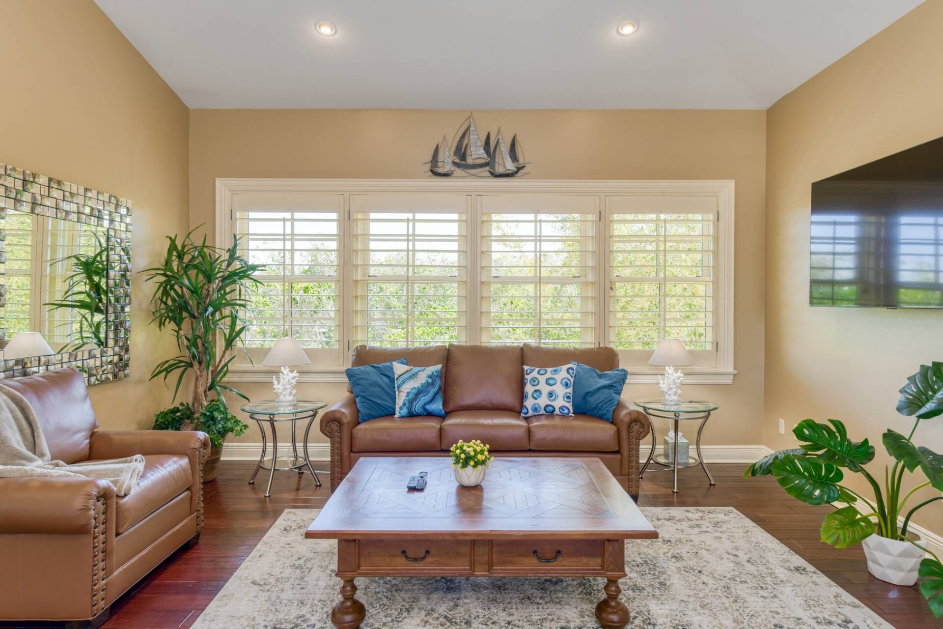 A living room with a brown leather sofa, a wooden coffee table, and a large window with shutters.