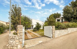 A residential property with a stone wall, a metal gate, and a paved driveway leading to a house with a white exterior.